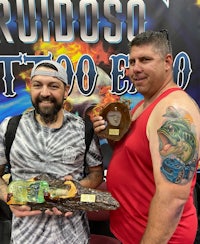 two men standing next to a sign that says rudoso tattoo expo